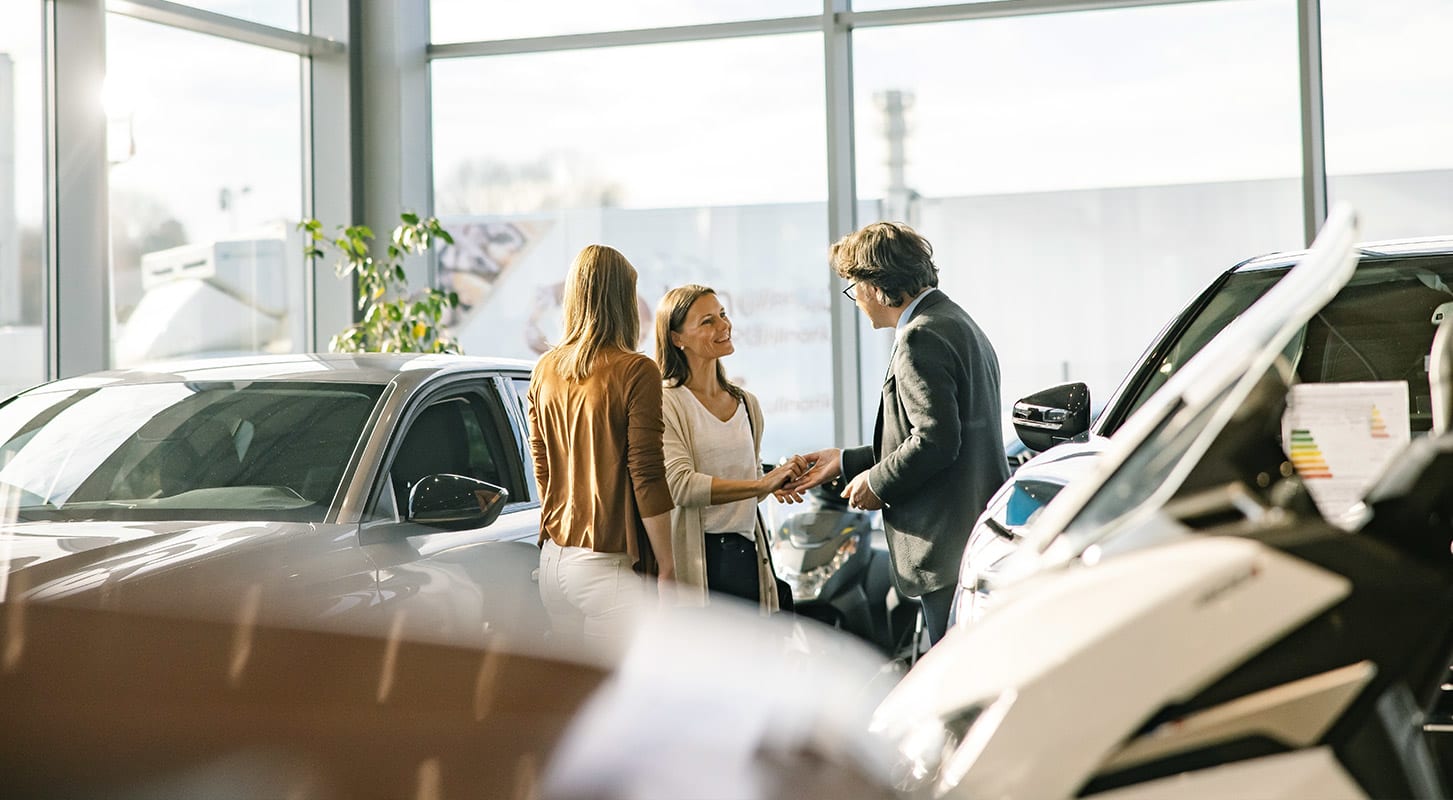 Two individuals engage in conversation with a salesperson inside a car showroom, exploring vehicle options together.
